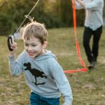 Father and son enjoying a sunny day flying a colorful kite together in a park.