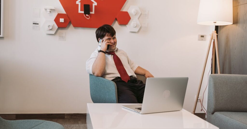 A man with Down syndrome smiling while on a phone call, seated in a modern office setting with a laptop.