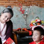A joyful family celebration with a grandmother and grandchildren sharing red envelopes indoors.