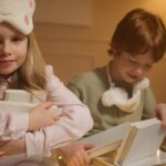 Two kids in pajamas enjoy bedtime stories in a cozy, warmly lit room.