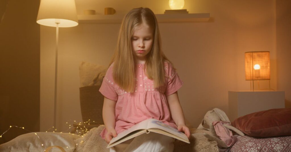 A young girl in a pink shirt reads a book in a warmly lit bedroom setting at night.