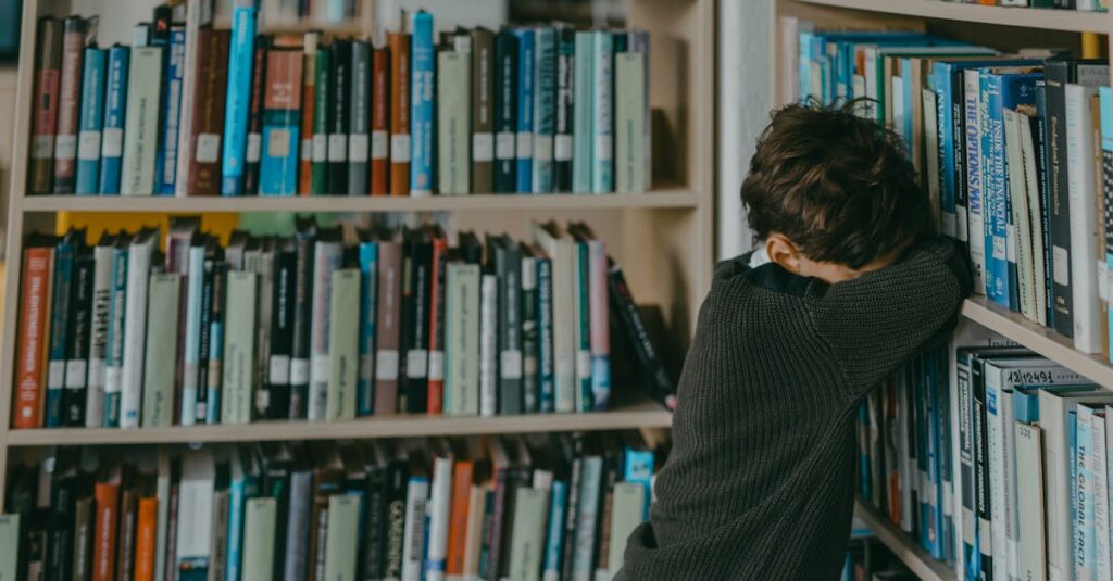 Young boy in a library, resting against a bookshelf, wearing a knitted sweater.