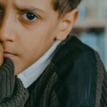 A young Middle Eastern boy looks concerned while standing in a library, showcasing emotions.