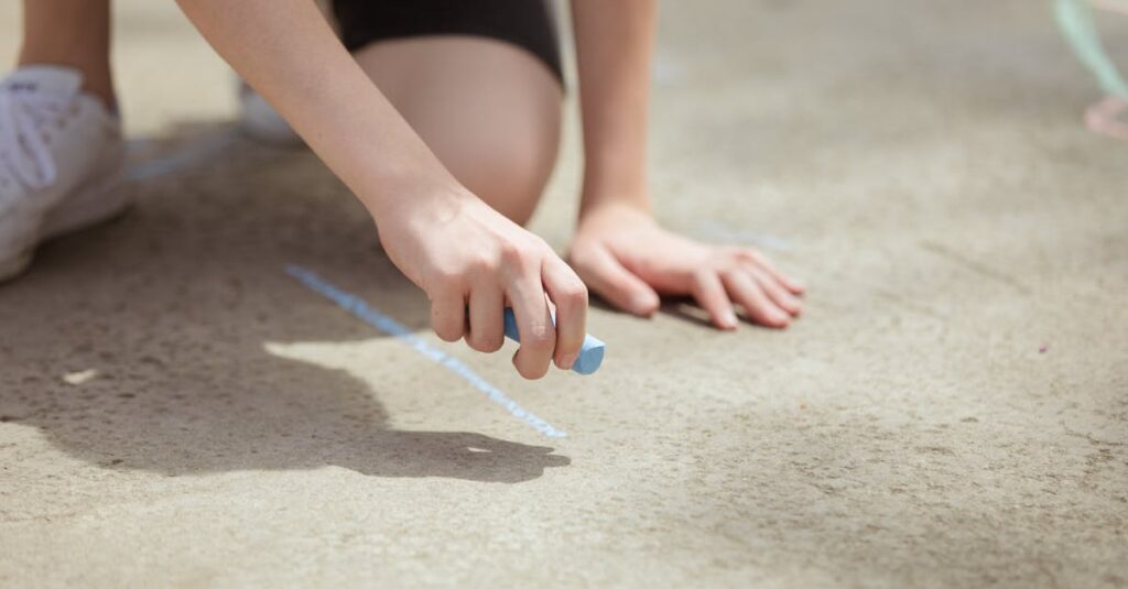 Young person drawing on outdoor pavement with colorful chalk.