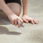 Young person drawing on outdoor pavement with colorful chalk.