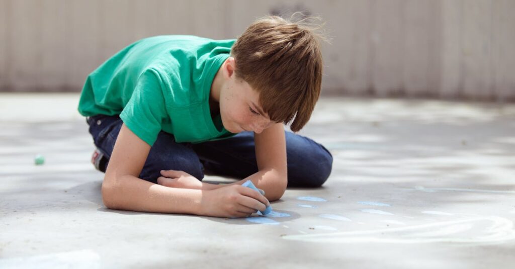 Child in a green shirt drawing on pavement with chalk during the day.