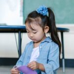 Young girl in a classroom setting, engaging with colorful paper toys, emphasizing early childhood education and creativity.