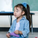 Cute young girl in a preschool classroom playing with colorful toys on a carpet.
