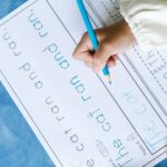 Child writing with pencil on a workbook page, focusing on handwriting education.