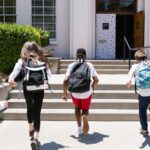 Group of students with backpacks running into school, captured from behind, showing excitement.
