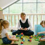 Children enjoying playtime with blocks and cardboard house in a cozy classroom.