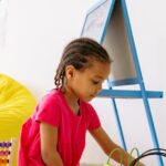 A child exploring an abacus and bead maze in a colorful classroom setting, encourages early learning.