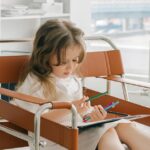 A young girl sitting and reading a book in a modern, well-lit library.