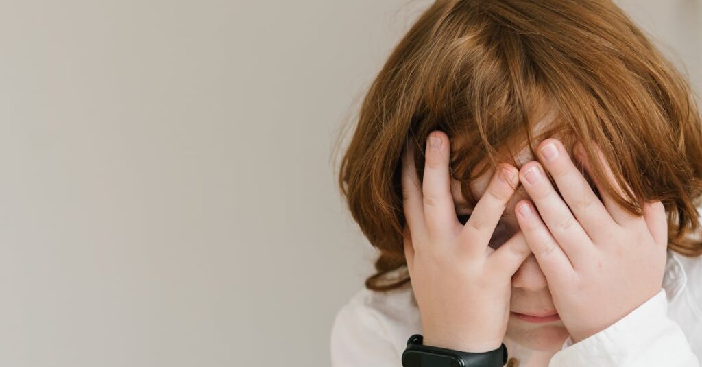 A shy child in a white shirt hiding their face indoors, conveying innocence and introspection.