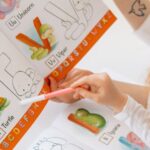 A child and adult learning alphabets using a colorful illustrated book and markers.