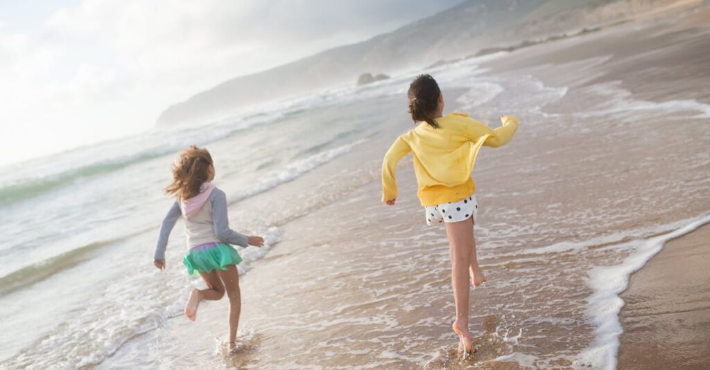 Two girls running along a scenic beach in Portugal, enjoying a sunlit day of fun and laughter.