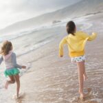 Two girls running along a scenic beach in Portugal, enjoying a sunlit day of fun and laughter.