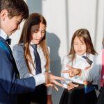 Group of diverse school children in uniform playing rock paper scissors indoors.