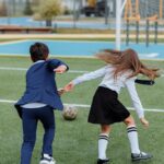 Two children in school uniforms playing soccer on a field, enjoying outdoor fun.