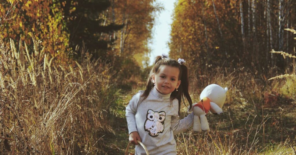 Young girl walking through a fall forest holding a basket and teddy bear.