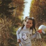 Young girl walking through a fall forest holding a basket and teddy bear.