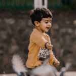A young boy joyfully playing among pigeons in an outdoor setting, capturing pure childhood happiness.