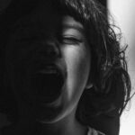A dramatic monochrome portrait of a child expressing emotion, captured in sunlight and shadow.