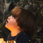 A young child gazes in wonder while holding a jar of lights in a magical forest setting, capturing innocence and curiosity.