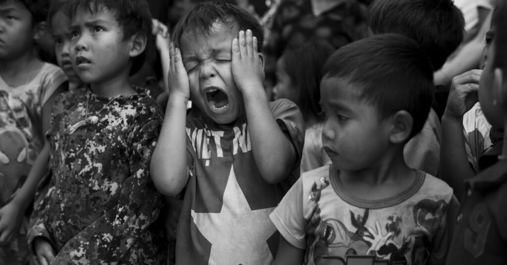 A group of children in a crowd, one appearing distraught, in a black and white setting.