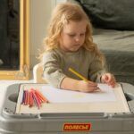 Young girl drawing with colored pencils at a play table in a cozy indoor setting.