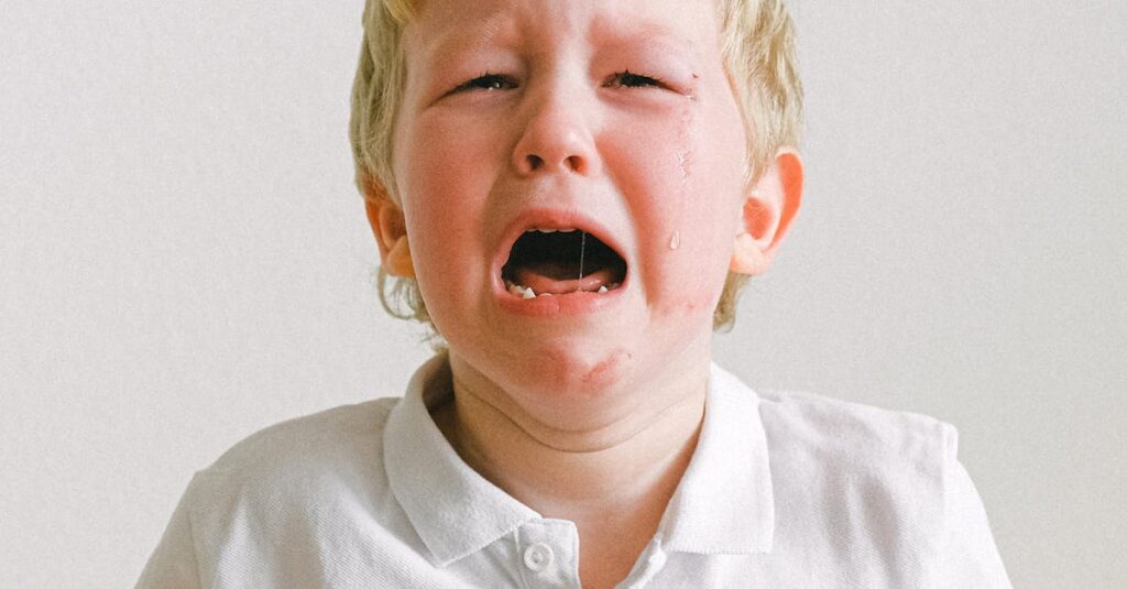 A young child crying, wearing a white shirt, showing strong emotions indoors.