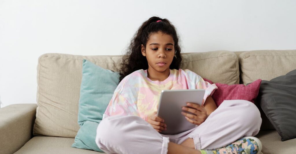 Teen girl sitting on sofa with a tablet, focusing on online learning indoors.