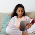Teen girl sitting on sofa with a tablet, focusing on online learning indoors.
