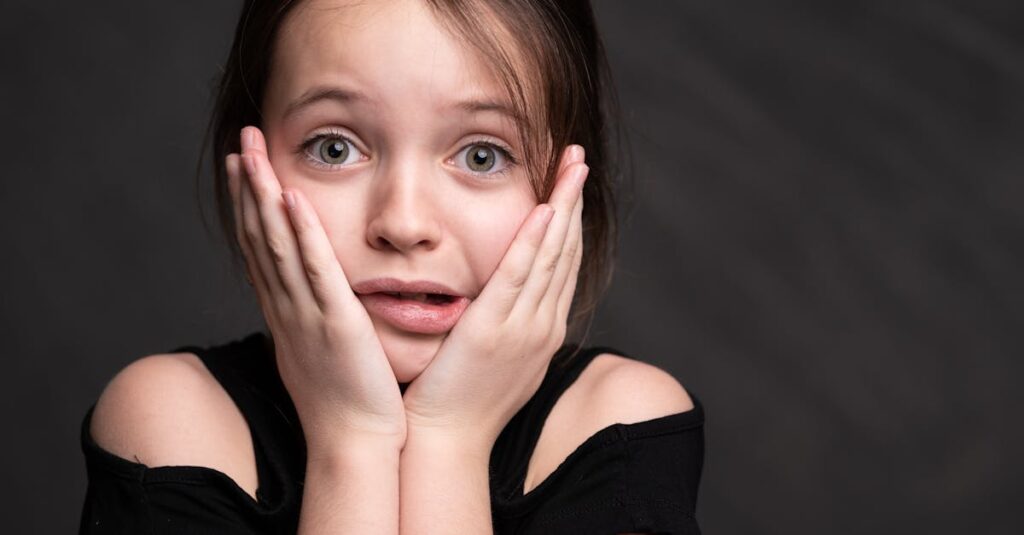 Portrait of a young girl in black top expressing surprise with hands on her face against a dark background.