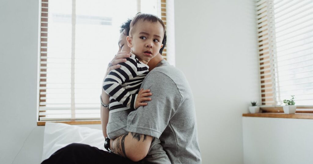 Father holding and comforting his young son by the window, showcasing warmth and family bond.