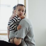 Father holding and comforting his young son by the window, showcasing warmth and family bond.