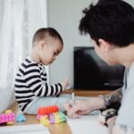 A father and son enjoy creative playtime, building blocks and drawing together indoors.