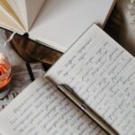 A serene writing setup featuring notebooks, a lit candle, and a laptop in a cozy indoor setting.