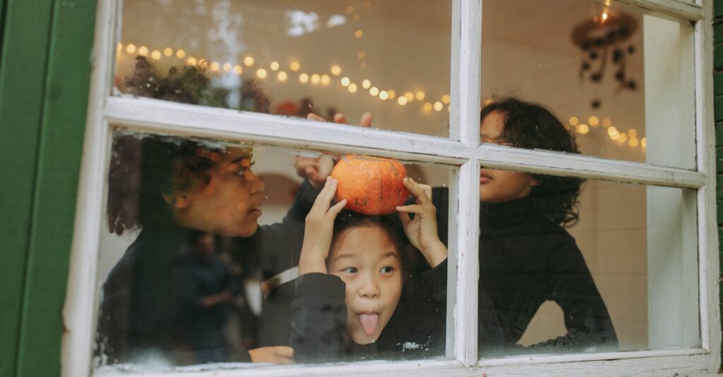 Playful children indoors celebrate Halloween with a pumpkin and festive lights.