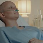 Bald woman in hospital bed receiving oxygen support, showing resilience in illness.