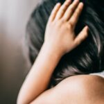 Young girl in emotional distress, sitting indoors with hand on head.