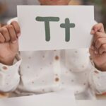 Close-up of child holding card with letter T in classroom, encouraging early education.