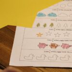 A child working on a simple math worksheet with colorful paper on a wooden desk.