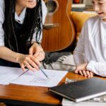 A woman teaching a young boy at a coffee table with papers and books, fostering learning and communication.