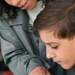 A woman helps a boy read in a classroom setting. Educational support concept.