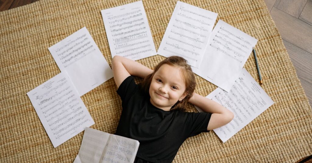 Cheerful girl in black dress lying on a carpet with musical sheets around her, enjoying a musical moment.
