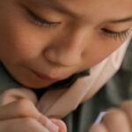 A young girl scout concentrates on writing in her notebook during an outdoor activity.