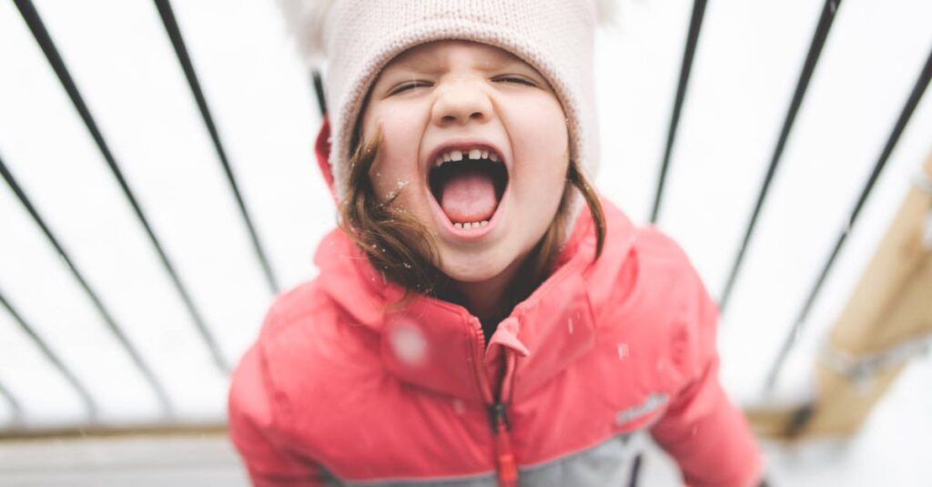 Cheerful child wearing winter clothing screams happily in the snowy outdoors.