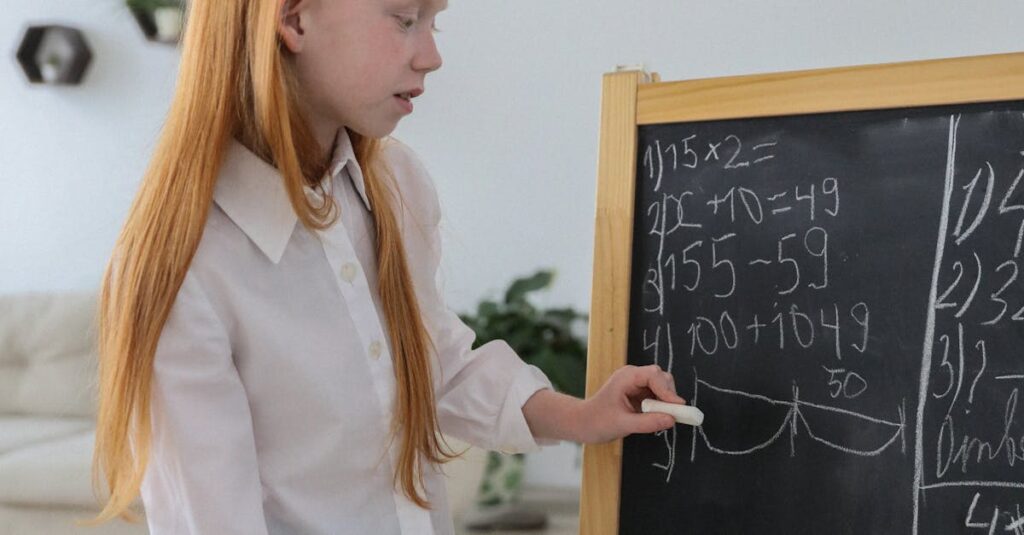 Concentrated schoolgirl standing near easel blackboard and writing mathematical equation in cozy light room