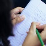 From above of crop anonymous diligent clever girl solving homework and writing in notepad